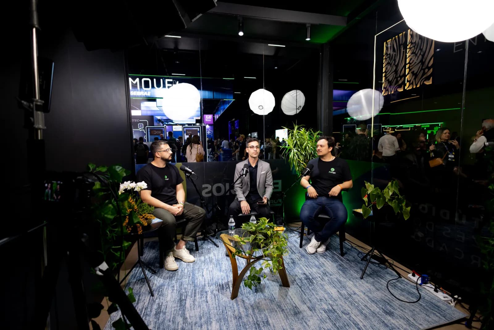 Estúdio Monking Play montado no Fórum E-Commerce Brasil: três pessoas gravando numa cabine de vidro, com o público do evento passando atrás
